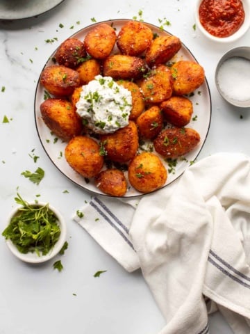 A plate of harissa roasted potatoes with a herbed white creamy dip on top.