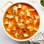 Soft tofu chunks in a bright orange-red sauce in a white pot.