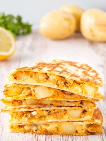 A stack of five cheesy potato quesadillas on white wood.