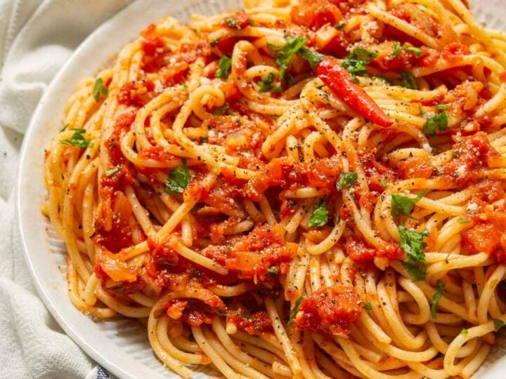 A white plate with spaghetti in a chunky tomato arrabiata sauce with a red chili pepper on top.