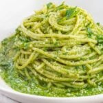 A spaghetti nest covered in green sauce in a white bowl.