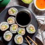 8 pieces of sushi with tofu and avocado on a grey plate with a small bowl of dark brown soy sauce.