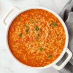 A white pot with orange-red sauce and rice with parsely sprinkled on top.