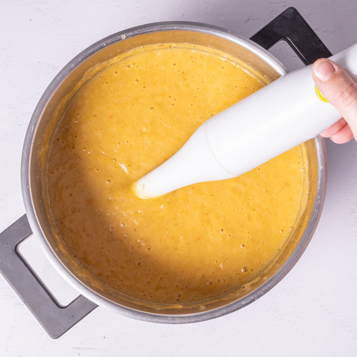 A stick blender in a pot with orange liquid.