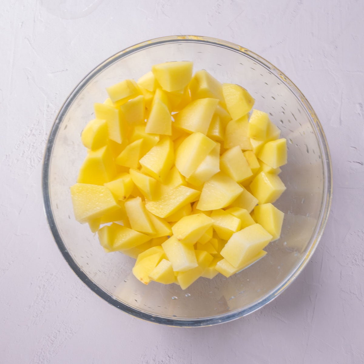A glass bowl full of peeled chopped potatoes.