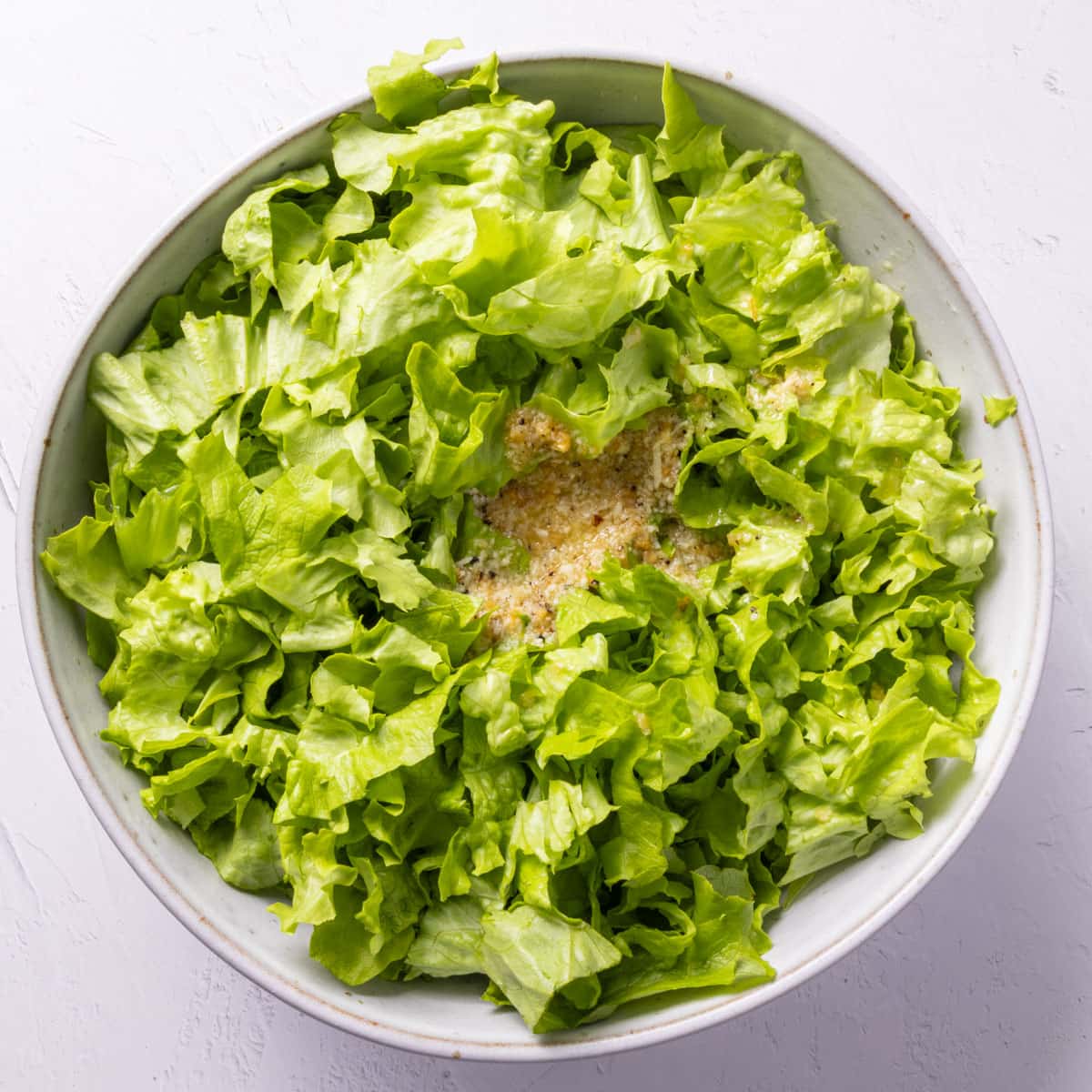 Green chopped salad leaves with dressing in the middle in a pale grey bowl.