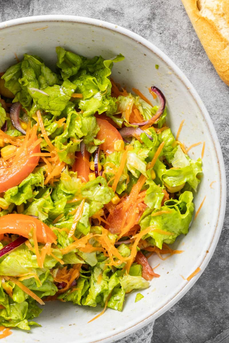 Salad in a bowl with tomatoes, onions, corn and lettuce.