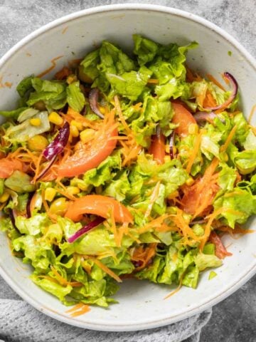 A grey bowl with mixed salad including lettuce, corn, tomatoes and olives.