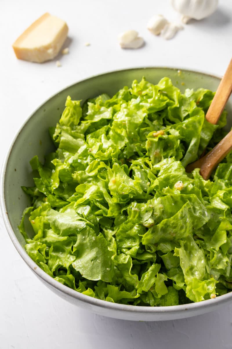 A bowl of chopped dressed greens with two wooden spoons and garlic and parmesan in the background.