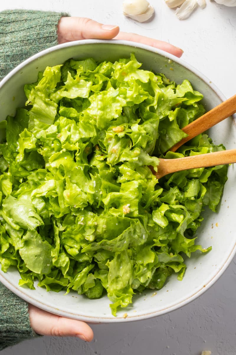 Two hands in a green jumper holding a bowl of green salad.