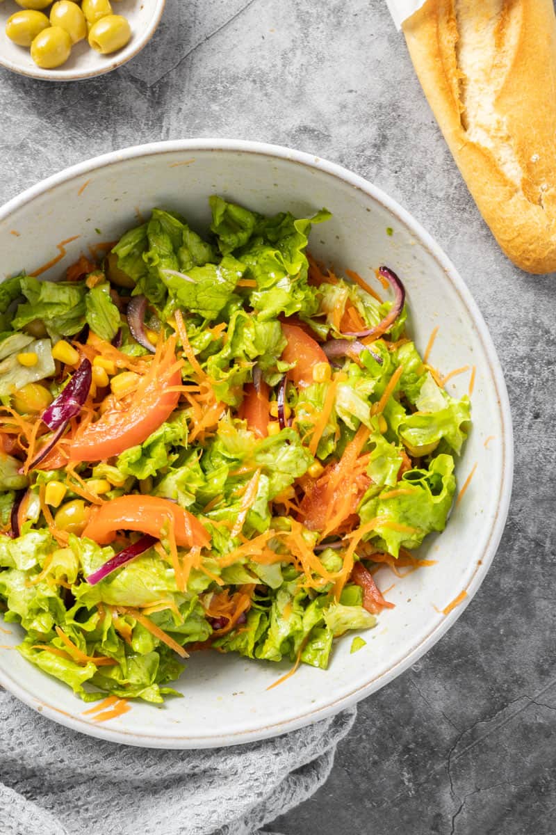 A bowl of olives, a baguette and a large bowl of salad.