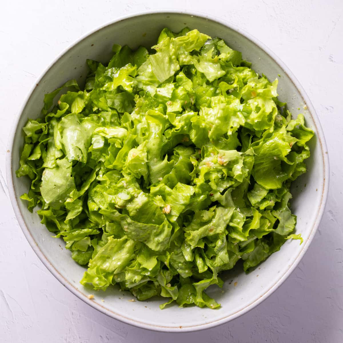 A bowl of green chopped dressed salad on a white backdrop.