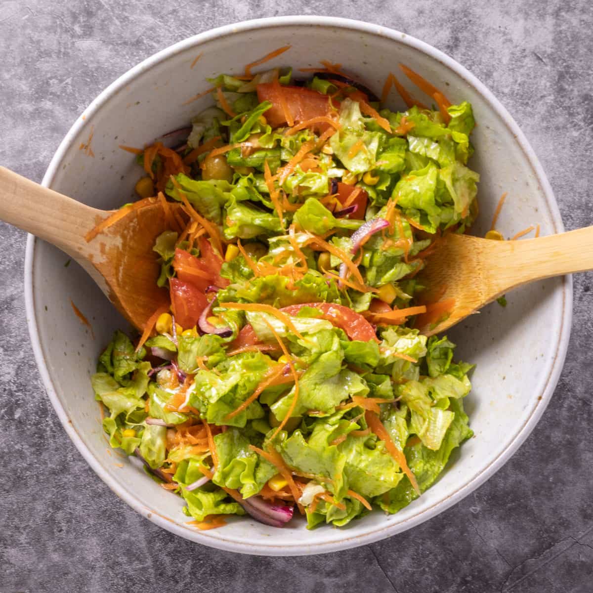 Two wooden spoons in a mixing bowl tossing a green mixed salad.