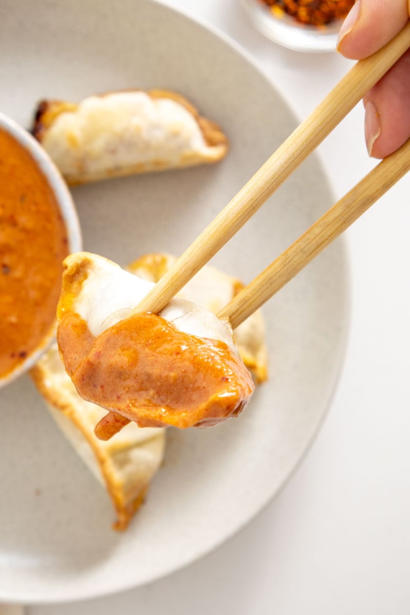 A gyoza dumpling held with chopsticks, partially covered in an orange sauce.