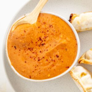 A bowl of thick orange sauce sprinkled with red pepper flakes.