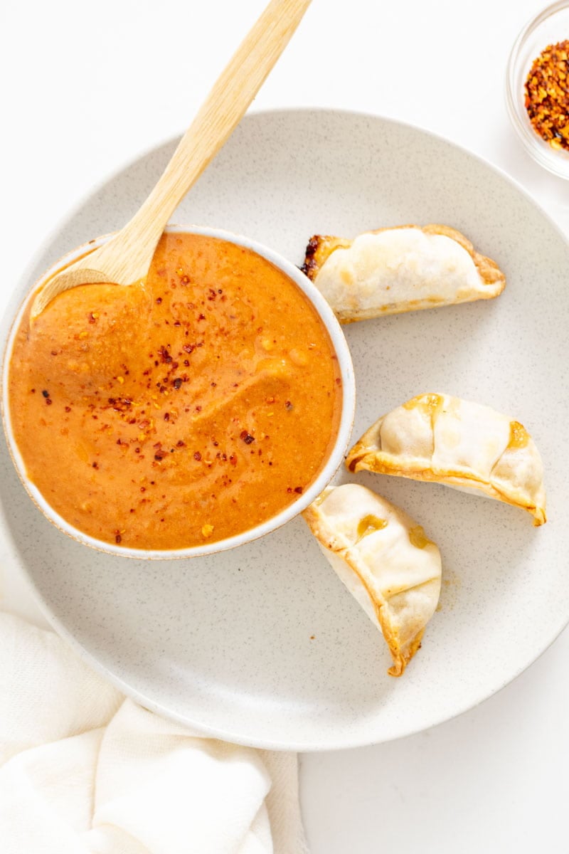 A bowl of orange sauce on a grey plate with three gyoza dumplings.