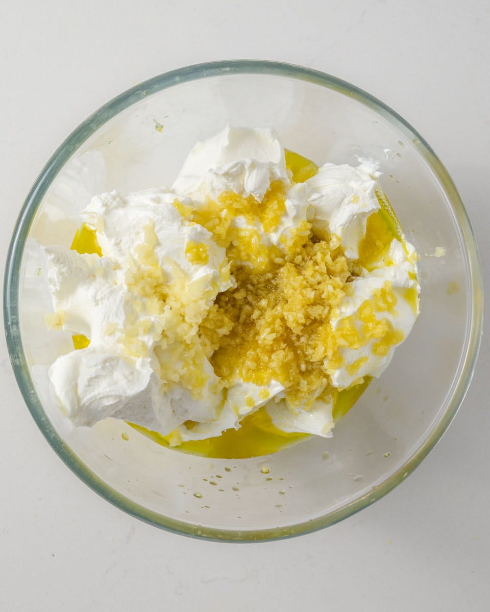 A glass bowl with thick white creamy liquid mixed with golden oil and chopped garlic.