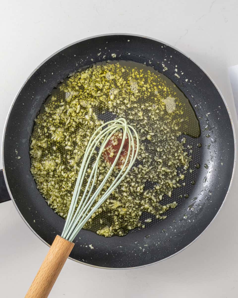 A whisk and oil and chopped garlic in a pan.