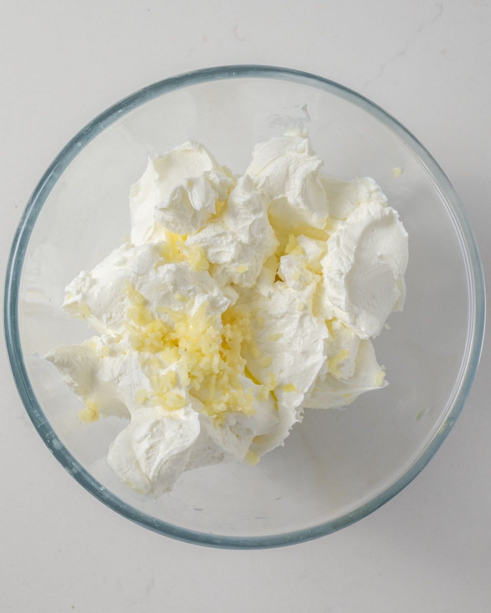 A glass bowl with thick white yogurt and chopped raw garlic on top.