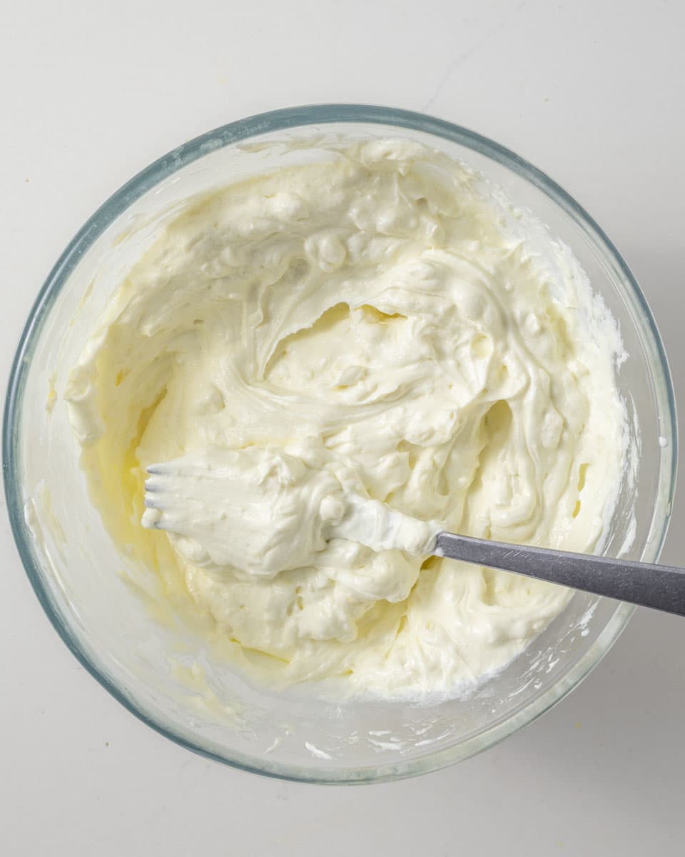 Whipped thick white creamy yogurt with a fork in a glass bowl.