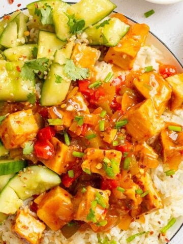 Chopped cucumber and chopped golden tofu pieces in a glossy orange sauce on rice.