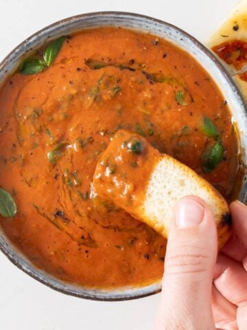 A grey bowl with a tomato sauce and small green basil leaves and bread being dipped into it.